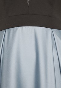 Robe avec un corsage noir et une jupe en satin bleu clair à plis. Texture lisse et sections de couleur contrastée.