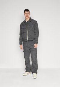 Γκρι τζιν μπουφάν με δύο τσέπες στο στήθος, συνδυασμένο με γκρι cargo παντελόνι και λευκά αθλητικά παπούτσια. Λείος υφασμάτινος χαρακτήρας, χρηστικός σχεδιασμός.