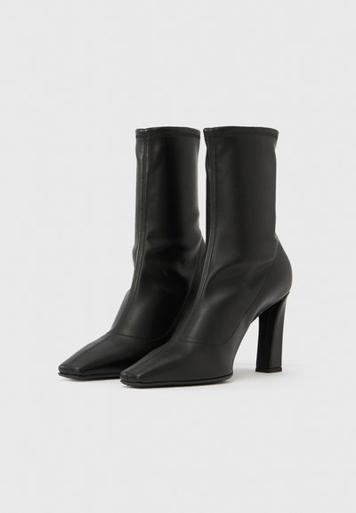 Melni īsie zābaki no gludas ādas ar cieši pieguļošu kājas daļu, smailu purngalu un masīvu augstu papēdi. Raksturo minimālas šuves.