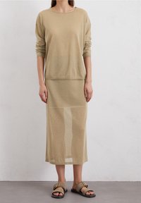 Beige gebreide top met lange mouwen gecombineerd met een bijpassende maxi rok. Beide kledingstukken zijn gemaakt van een lichte, doorzichtige stof. Minimalistisch ontwerp, geen patronen.