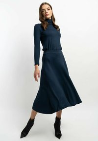 Navyblauer Rollkragenpullover aus weichem Stoff, kombiniert mit einem passenden, ausgestellten Rock. Das Outfit zeichnet sich durch eine glatte Textur und subtile Formdetails aus.