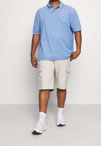 Polo de color azul claro con mangas cortas y cuello, combinado con pantalones cortos de carga beige con bolsillos laterales y zapatillas blancas.