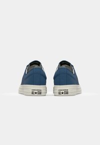 Blue canvas shoes with white rubber soles, featuring a low-top design, lace-up front, and "Converse All Star" branding on the heel.