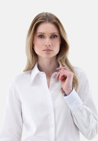 Camicia button-up bianca in cotone con colletto classico, polsini azzurri a contrasto e delicati dettagli di cucitura lungo le cuciture.
