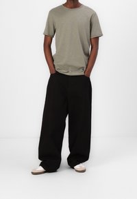 Olijfgroene T-shirt met korte mouwen en een ronde hals, gecombineerd met loszittende zwarte broek en lichtgekleurde sneakers. Eenvoudige, casual stijl.