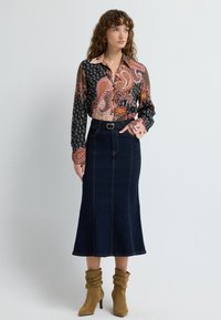 Bluzka z długim rękawem w wzory w kolorze czarnym, różowym i pomarańczowym, zestawiona z ciemnoniebieską spódnicą do kostek z paskiem w talii i widocznymi przeszyciami.