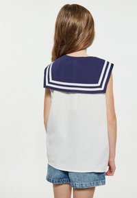 Mørkeblå sømandskrave med hvide striber; hvid ærmeløs top; denim shorts. Bagfra, glat stof, afslappet design.