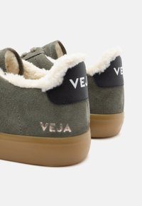 Zöld velúr tornacipők műszőrme bélésben, fekete bőrből készült sarokdíszítéssel és kaucsuk talppal. A "VEJA" logó fényes kivitelben található.