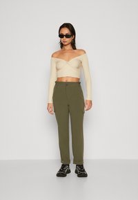 Top corto a coste color beige, scollato sulle spalle, con un dettaglio a nodo davanti, abbinato a pantaloni cargo verdi con tasche laterali e chiusura a bottoni. Sneakers nere.