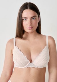 Soutien-gorge en dentelle rose clair avec un décolleté plongeant, des bords festonnés et des bretelles ajustables. Le motif texturé sur l'ensemble du tissu ajoute du détail.