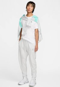 Hvid T-shirt og lys grå joggingbukser med elastisk linning. En let grå og mintfarvet jakke er draperet over skuldrene. Hvide sko.