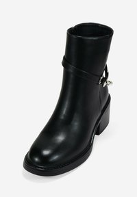 Bota de cuero negro hasta el tobillo con punta redondeada, tacón cónico, cremallera lateral y una correa decorativa con un acento de hebilla. Textura suave.