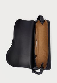 Μαύρη δερμάτινη τσάντα με καμπυλωτό σχέδιο, διαθέτει καφέ εσωτερικό, τσέπη με φερμουάρ και μια δομημένη λαβή στο πάνω μέρος για εύκολη μεταφορά.