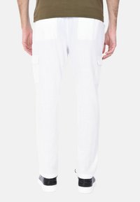 Pantaloni cargo bianchi con due tasche laterali, caratterizzati da un design a gamba dritta e una texture morbida. Indossati con sneakers nere.