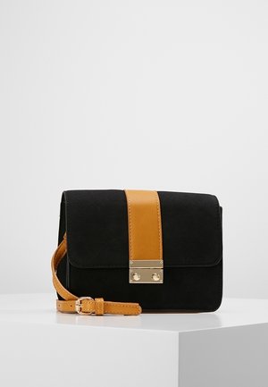 Zwart-bruine leren crossbodytas met gouden gesp en verstelbare riem, tentoongesteld op een wit voetstuk tegen een eenvoudige achtergrond.