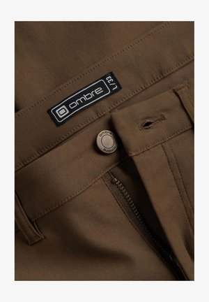 Brown fabric trousers with a front zipper and button closure. Features an "ombre" label and standard stitching details.