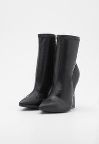 Bottes noires à chevilles avec une finition en cuir brillant, orteils pointus et un talon compensé haut. Comprend une fermeture éclair sur le côté.