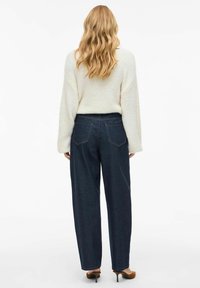 Light, textured sweater in cream color paired with high-waisted dark blue wide-leg jeans. Features back pockets and a relaxed fit.