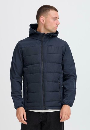 Chaqueta acolchada de color azul marino con cremallera frontal, capucha ajustable y bolsillos laterales. Textura suave con detalles de costura horizontal.