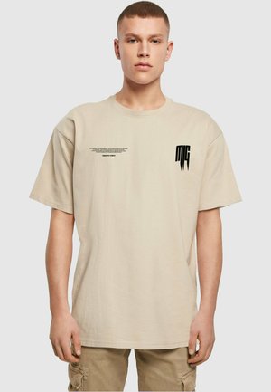 T-shirt en coton beige avec une coupe décontractée, présentant un design de texte imprimé noir et un logo à l'avant. Manches courtes et col rond.