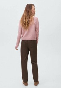 Suéter de punto rosa claro con dobladillo acanalado, combinado con pantalones oscuros de textura marrón. Mostrado desde la parte trasera, mostrando un ajuste casual.