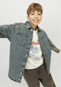 Denimjacka med krage, två bröstfickor och silverknappar. Ljusblå färg med en texturerad yta. Bärs över en grafisk sweatshirt.