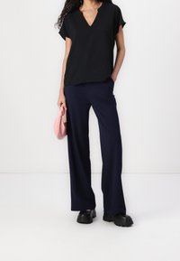 Haut noir à manches courtes avec un décolleté en V, associé à un pantalon large bleu marine. Une pochette rose apporte un contraste. Les chaussures ont des semelles noires épaisses.