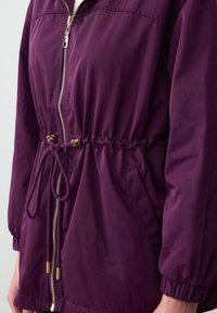 Paarse windjack met een taille die aansnoert, gouden rits, elastische manchetten en zijzakken. Glad, lichtgewicht materiaal met een ontspannen pasvorm.