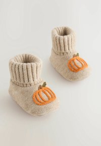 Chaussons pour bébé en tricot beige doux avec des poignets côtelés et une broderie de citrouille orange sur les orteils, posés sur une surface claire.