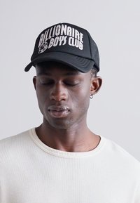 Schwarze Kappe mit weißem "Billionaire Boys Club"-Text, Netzrücken, gebogener Schirm, getragen mit einem strukturierten cremefarbenen Langarmshirt.