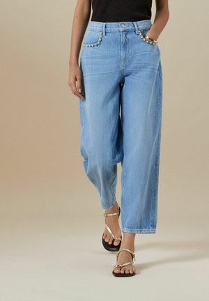 Jeans largi de culoare albastru deschis, cu buzunare frontale. Prezintă cusături decorative de-a lungul marginilor buzunarelor. Asortați cu sandale argintii cu barete.