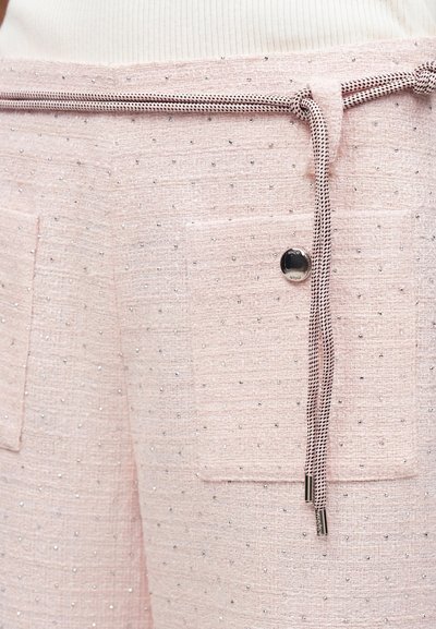 Ανοιχτό ροζ υφασμάτινο παντελόνι με μικρά ασημένια τρουκ, δύο μπροστινές τσέπες, ένα μαύρο κουμπί και ροζ ζώνη με κορδόνι δεμένη κόμπο.