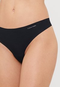 Svart Calvin Klein stringtrosa med en sömlös design och en diskret logotyp, tillverkad av ett glatt, elastiskt material. Minimalistisk klipp och stil.