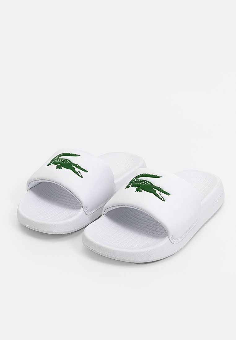 Sandales blanches à glissière avec un semelage texturé, arborant un logo de crocodile vert sur la sangle. Fabriquées en matériau synthétique, avec un design flexible.