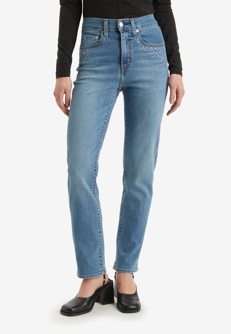 Ljusblå högmidjade jeans med rak benöppning, prydda med nitar nära framfickorna, tillverkade av denimstoff.