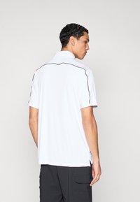 Polo blanc avec col, orné de liserés noirs le long des épaules et des côtés. Texture lisse, manches courtes et coupe décontractée.