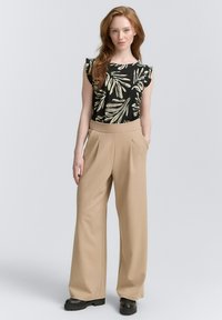 Top nero con motivo a foglie verdi, abbinato a pantaloni beige larghi, con vita alta e gambe ampia. Tessuto texturizzato, accenti minimali.