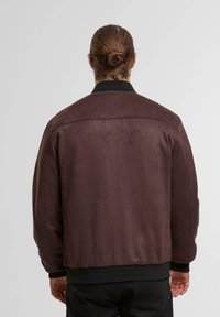 Jackă din suede maro cu guler negru, manșete cu nervuri și o textură netedă. Prezintă o croială dreaptă și un design simplu la spate.