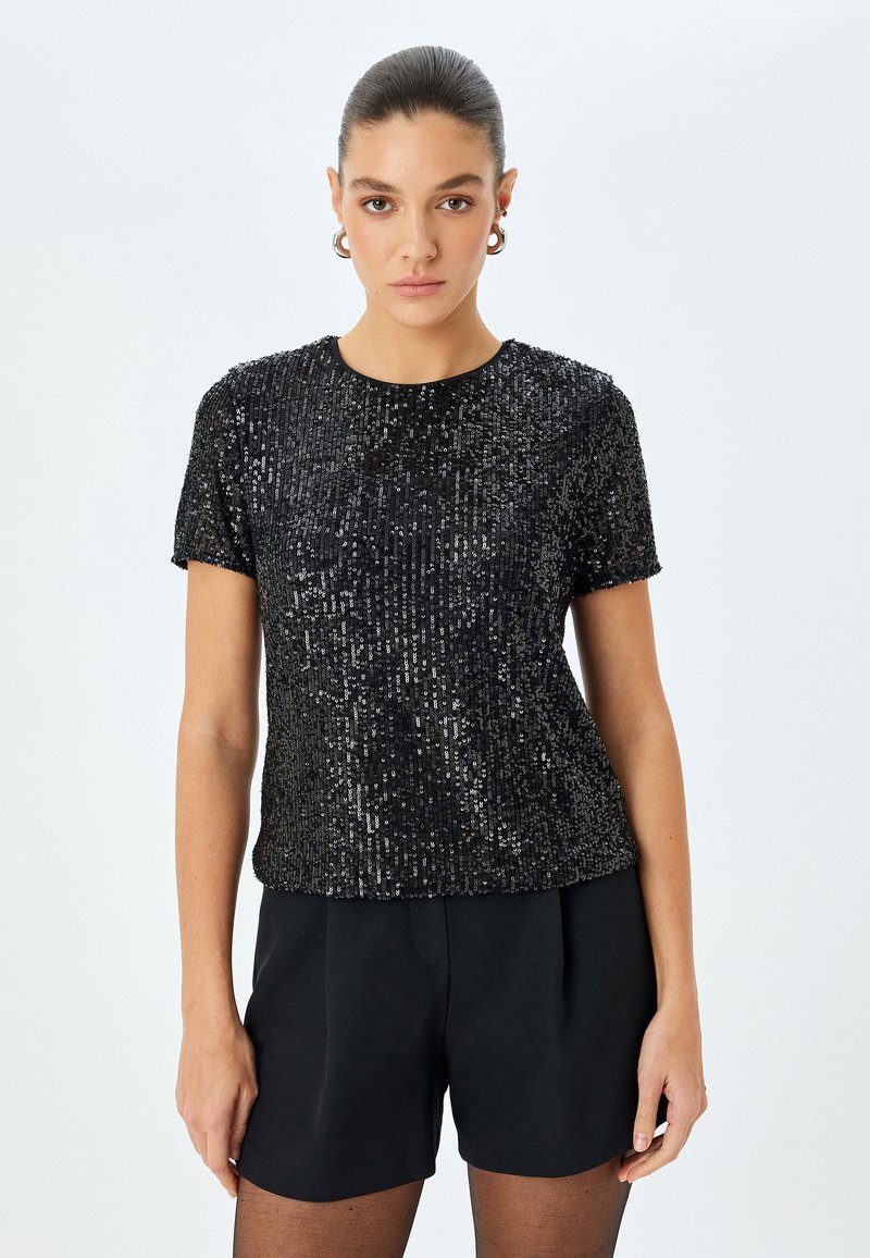 Zwart sequined cropped top met korte mouwen en een ronde halslijn, met een gestructureerd oppervlak en een losse pasvorm, gecombineerd met zwarte shorts.
