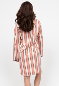 Abito a righe in rosa chiaro e bianco, con maniche lunghe, vestibilità comoda e orlo arrotondato. Le righe sono accentuate da linee dorate.