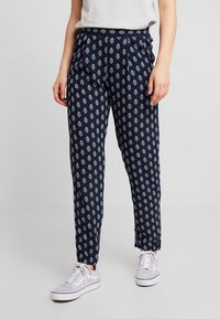 Granatowe spodnie we wzory z białymi geometrycznymi motywami, wykonane z lekkiego materiału. Charakteryzują się luźnym krojem i zwężanymi nogawkami, stylizowane z białymi trampkami.
