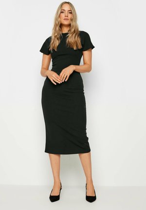 Robe midi noire ajustée avec des manches courtes, texture douce et silhouette élégante, assortie à des talons noirs.