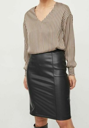 Femme portant un chemisier à manches longues à motifs, rentré dans une jupe crayon en cuir noir arrivant au genou.