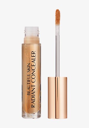 Open tube of beige liquid concealer with gold cap and applicator wand coated in product on a white background.