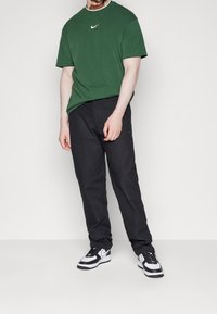 Green cotton t-shirt with a white neckline and Nike logo, paired with black trousers and white sneakers featuring black accents.