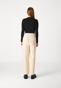 Top lungo a maniche nere a costine abbinato a pantaloni beige a gamba larga con vita alta, dotati di una cintura elasticizzata e due tasche posteriori. Scarpe nere.