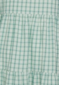 Vestido em gingham verde-claro com quadrados alternando entre tons claros e escuros, com camadas franzidas e um tecido macio e texturizado.
