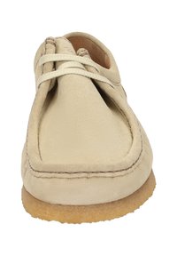 Beige Wildlederschuh mit runder Spitze und einem Obermaterial mit überkreuzten Schnürsenkeln, ergänzt durch eine strukturierte Gummisohle und Kontrastnähte.