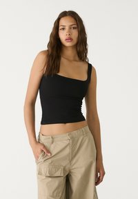Black cropped tank top with a one-shoulder design, made from smooth, stretchy fabric. Paired with beige cargo pants featuring side pockets.