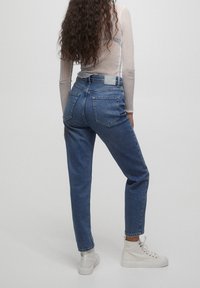 Jeans de mezclilla de cintura alta en azul medio con corte recto. Presentan bolsillos traseros y una etiqueta gris claro en la cinturilla.